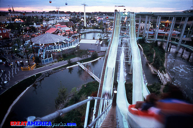 Yankee Clipper chutes
Gurnee, IL
This Gurnee photo holds many memories for me because I used to work on the Yankee Clipper there. This was the view from the chutes operator's position. To get here, we could either walk along the lower flume, climb the second lift and walk the upper flume to the chutes position, or we could climb the steep catwalk you see here. One of the funniest things about working the chutes position was seeing the expressions on the faces of guests as they were about to take the big plunge. Also visible in this photo are two of the other main rides that I worked at Gurnee: the Southern Cross and Eagle's Flight skyrides.
Keywords: Gurnee