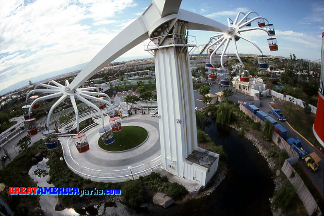 massive Sky Whirl
Santa Clara, CA
This unusual shot gives some idea of the immensity of the Sky Whirl. It also shows the keys to the mechanical operation of the massive ride. Atop the "tree" pylon, the three arms joined at a hub that rotated like a turntable. This rotating hub was on a giant hinge that allowed the hub to be raised and lowered by a huge hydraulic system. The hydraulics are seen here on the right, below the hub. On the left, below the hub, are some of the motors used to rotate the arms. To lower a wheel to the ground, the hydraulics were used to tilt the hub upward. Somewhat surprisingly to the casual observer, the system was at rest with all three wheels in the air. After closing time, Sky Whirl was usually parked for the night with all three wheels up in the air. 
